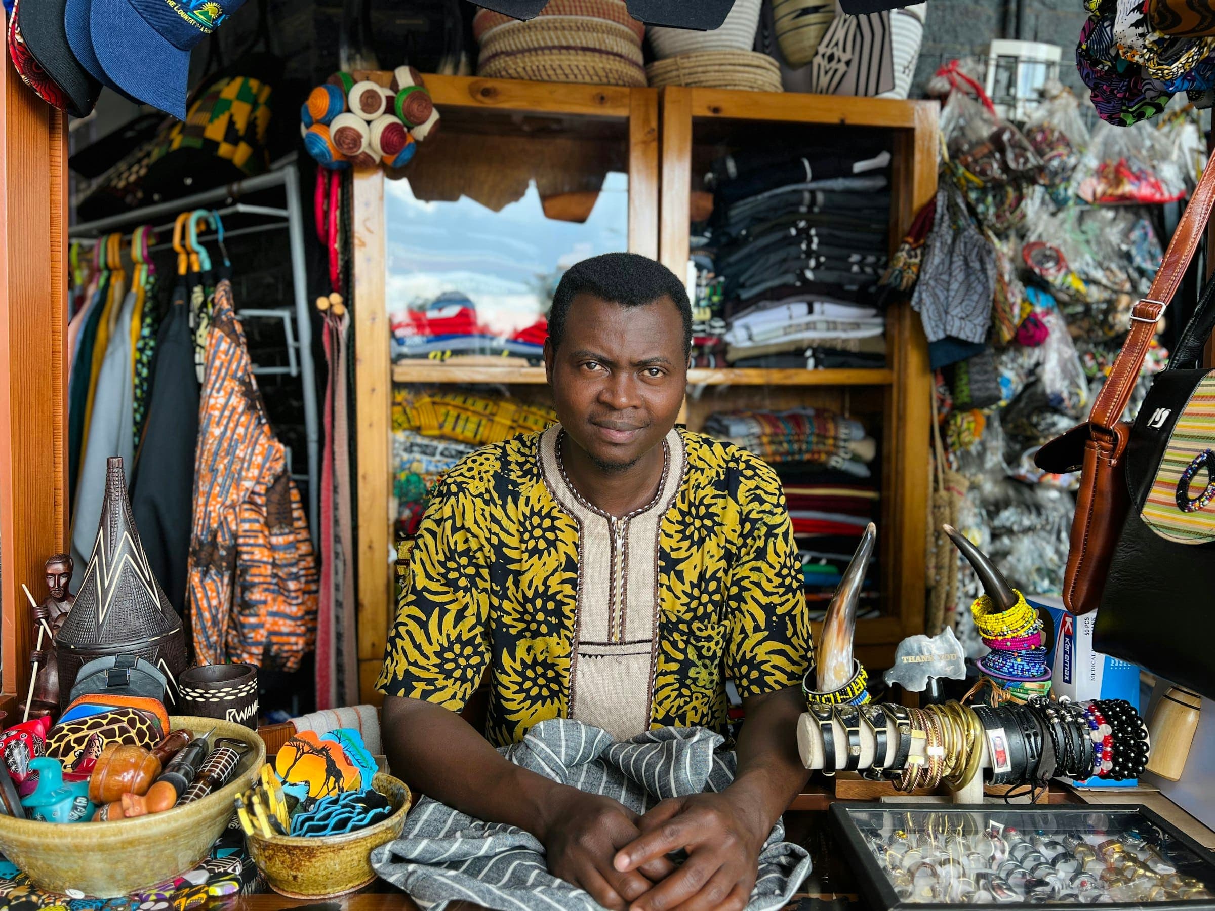 Shopkeeper sits inside a boutique stocked with clothing, fabrics and handmade crafts