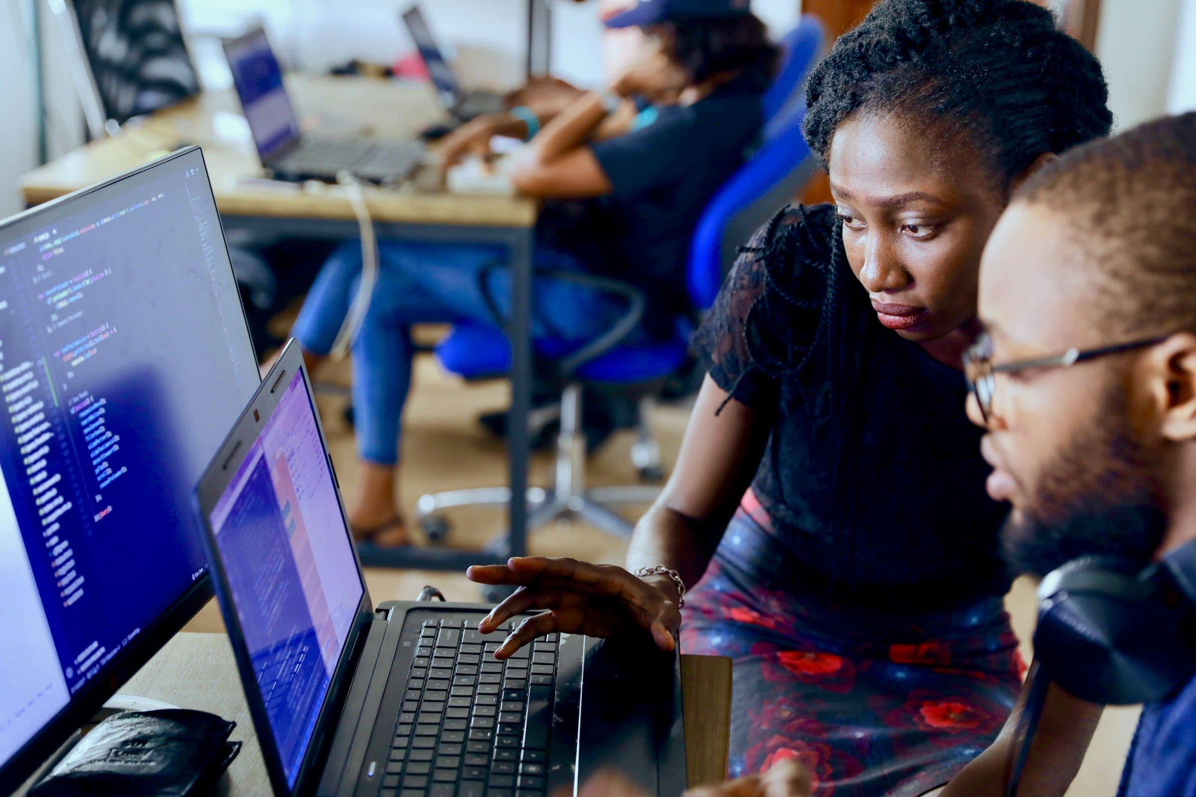 Two colleagues collaborate at a computer in a busy tech startup office